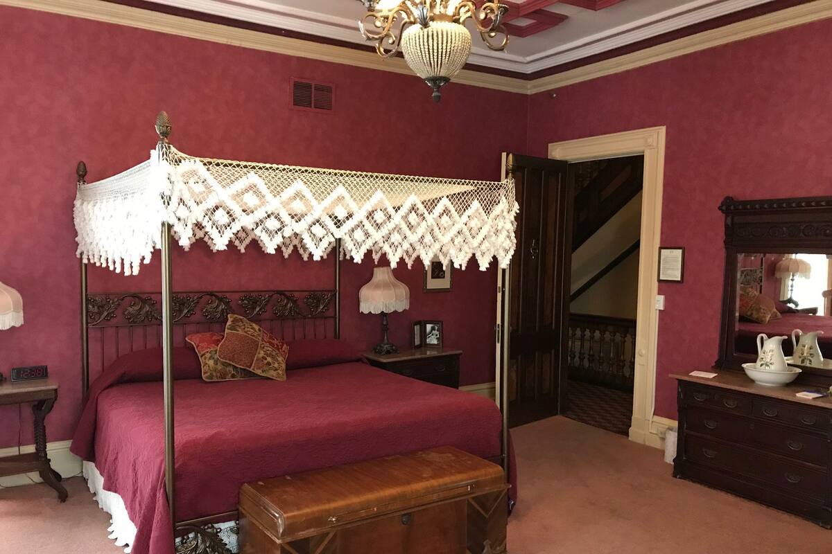 A four-poster bed with a canopy, a wooden chest, a nightstand, a dresser, and a mirror.