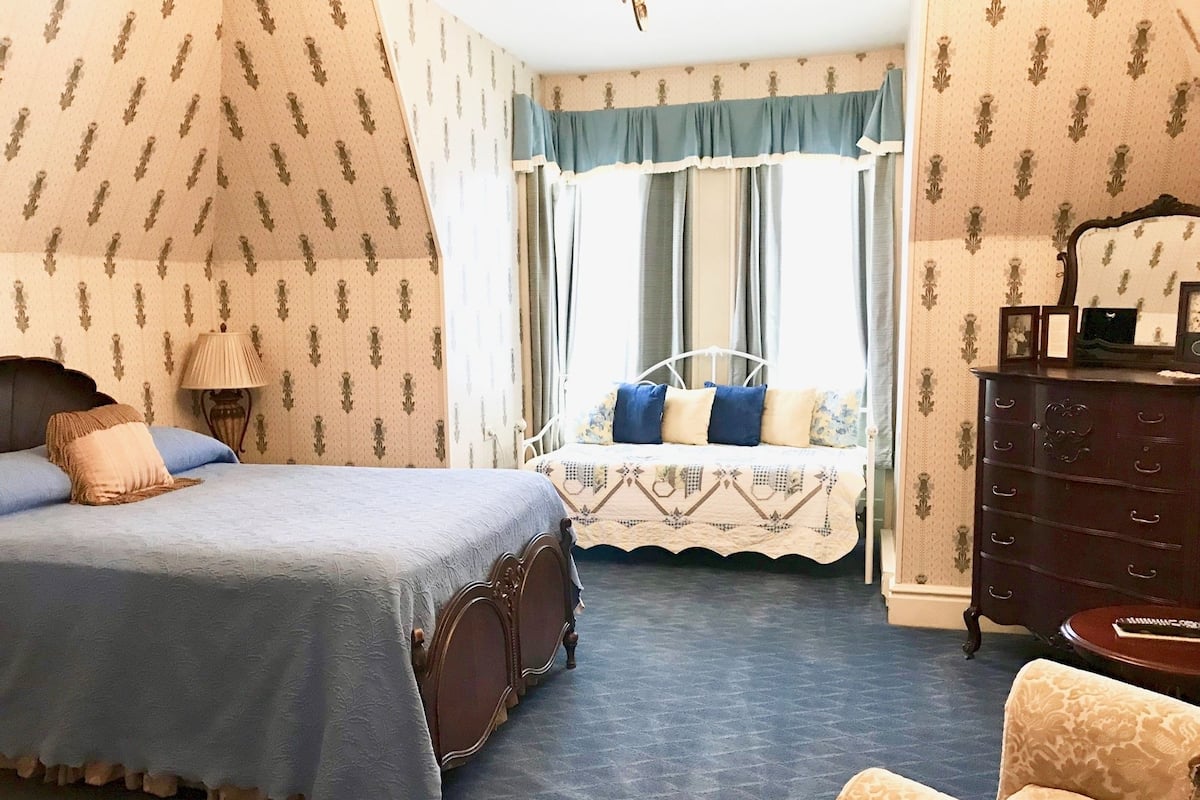 A bedroom with a bed, a dresser, a chair, and a window with curtains.