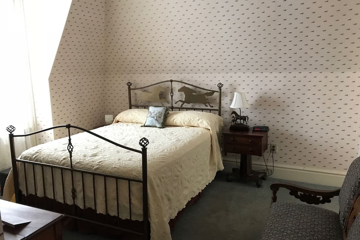 A bedroom with a bed, a nightstand, a chair, and a patterned wallpaper.