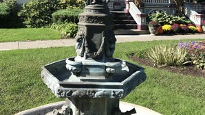 A statue in a garden with a large, ornate building in the background. - Batcheller Mansion Inn (Saratoga Springs)