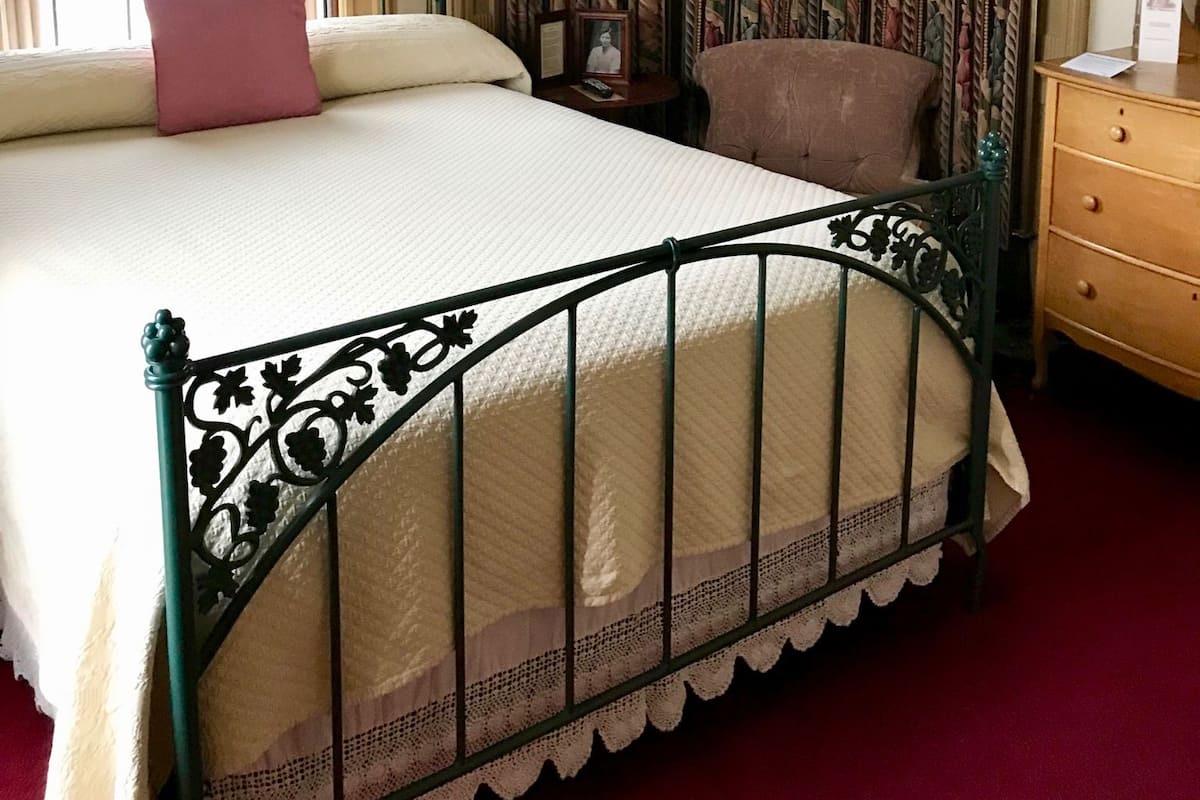 A bedroom with a bed, a chair, a nightstand, and curtains.