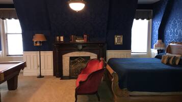 A bedroom with a large bed, a red chair, a fireplace, and a chandelier.