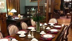 A formal dining room with a long table set for a meal, surrounded by chairs with striped upholstery. - Batcheller Mansion Inn (Saratoga Springs)
