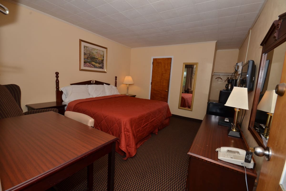 A hotel room with a bed, a desk, a telephone, a lamp, a mirror, and a painting on the wall.