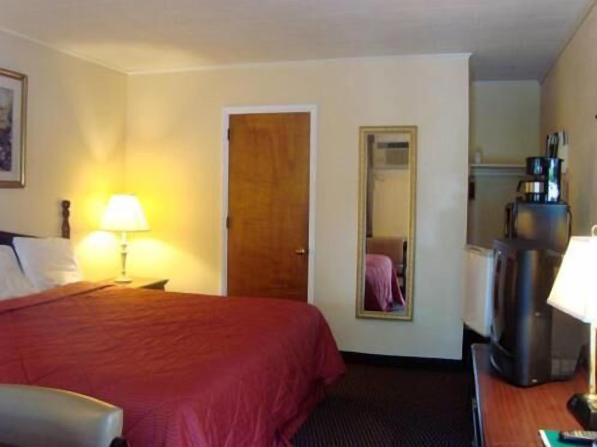 Una habitación de hotel con cama, escritorio, cafetera y espejo.