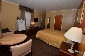 A hotel room with a bed, a desk with a lamp, a small refrigerator, a television, and a window with curtains. - Budget Host Mel-Dor Motel (New Berlinville)