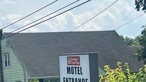 Une enseigne à l’entrée d’un motel, portant le logo de la chaîne Budget Inn, un panneau de rue indiquant « Spring Garden Dr. », et un cône de signalisation.