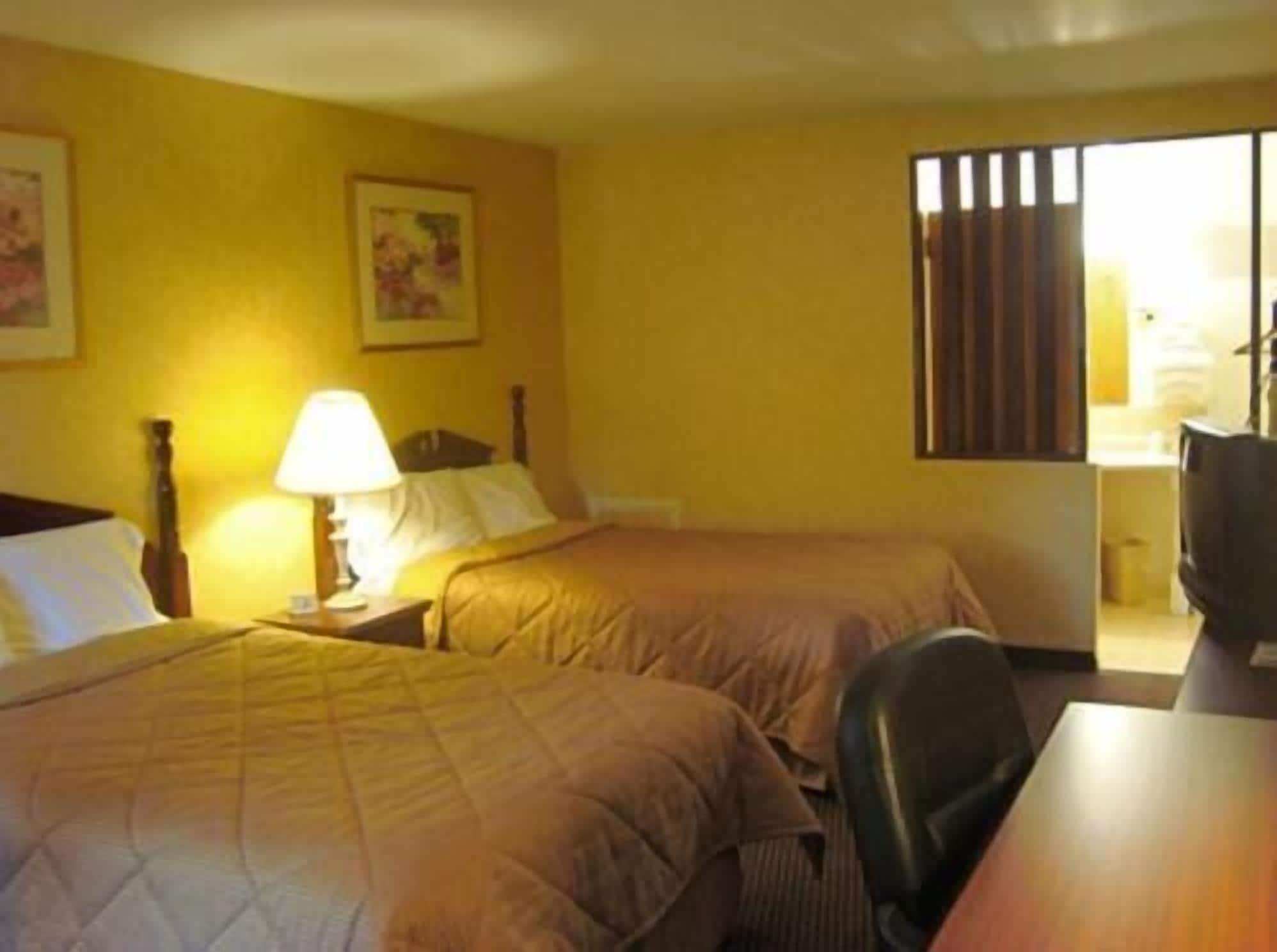 A hotel room with two beds, a desk, and a chair.