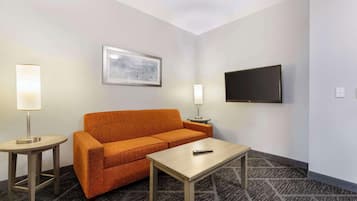 Habitación de hotel con sofá, una mesita, control remoto, televisor de pared y dos lámparas de noche.