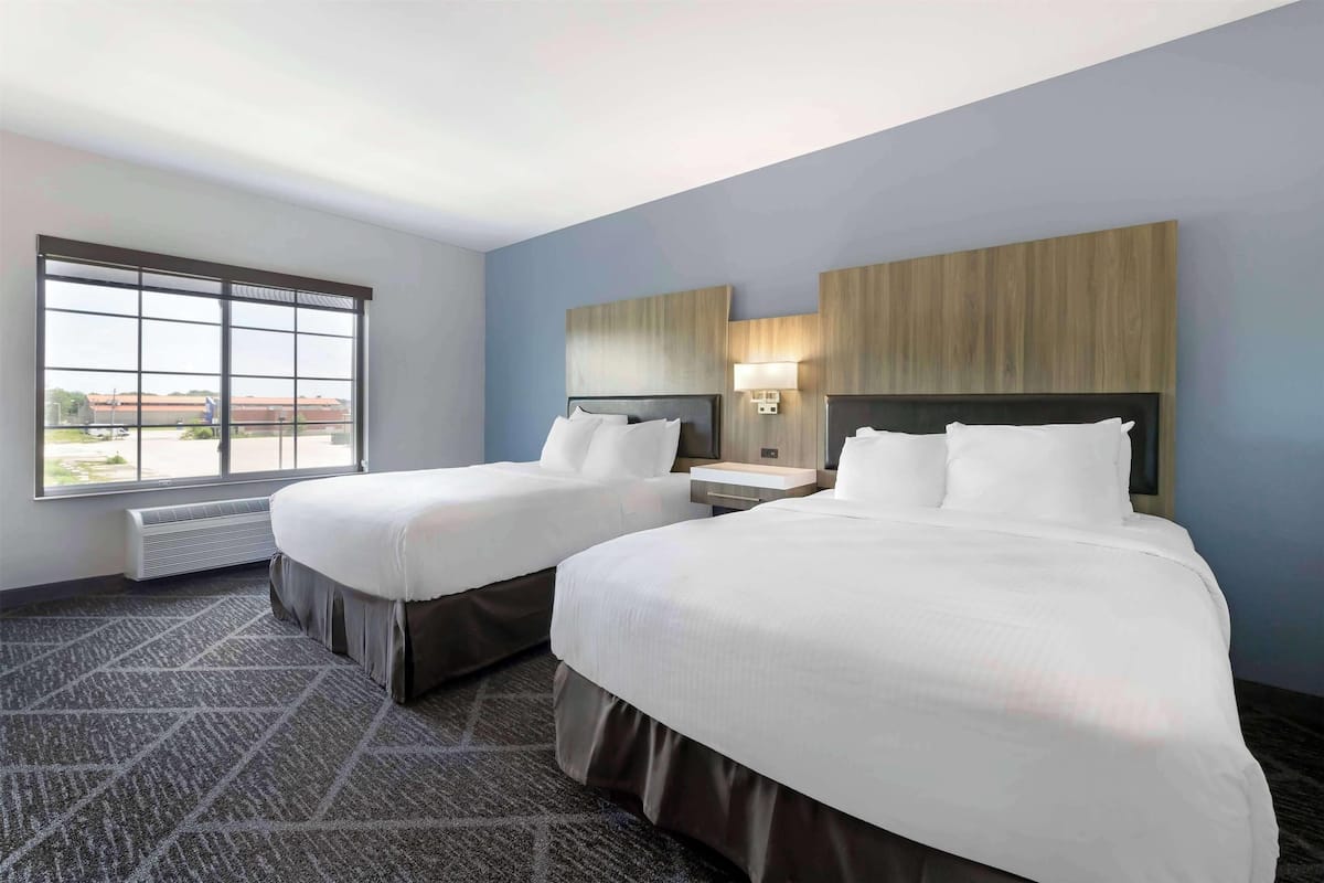 A hotel room with two beds, a large window, a wall-mounted TV, and a nightstand.