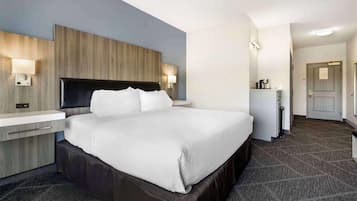 A modern hotel room with a large bed, bedside tables, a built-in desk, and a small kitchenette.
