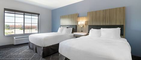 A hotel room with two beds, a large window, a wall-mounted TV, and a bedside table.