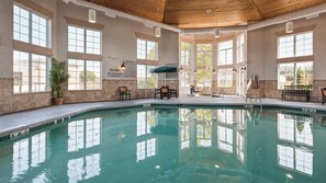 An indoor swimming pool with clear water, surrounded by large windows and a wooden ceiling.