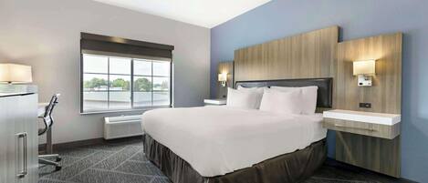 A hotel room with a large bed, a desk, a chair, a window with a view, and a wall-mounted light.