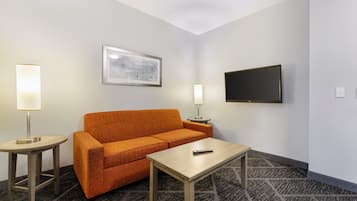 A hotel room with a sofa, a small table, a TV, and two bedside lamps.