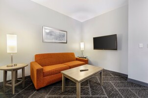 Een hotelkamer met een sofa, een tafeltje, een televisie en twee bedlampjes.