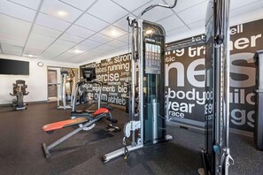 A gym with various exercise equipment, a wall with motivational words, and a ceiling with recessed lighting.