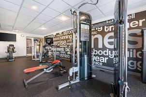 Un gimnasio con diversos equipos de ejercicio, una pared con mensajes motivacionales e iluminación empotrada en el techo.