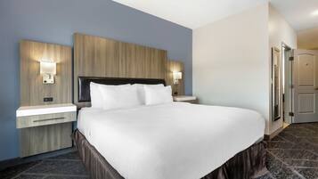 Una habitación de hotel con una cama grande, dos mesitas de noche con lámparas, un cabecero de madera y suelo alfombrado.