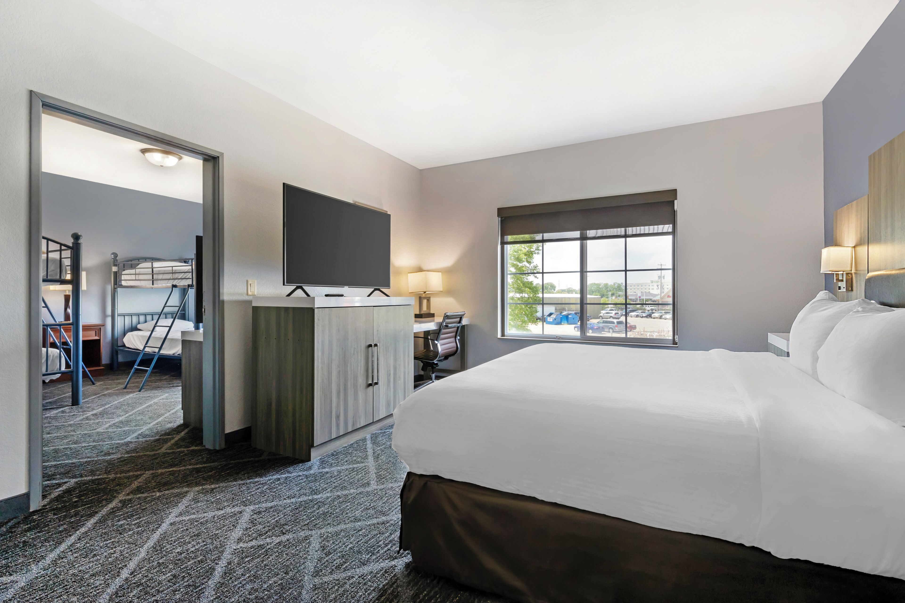 Habitación de hotel con una cama grande, un escritorio con silla, un televisor montado en la pared y una ventana con vistas al exterior.