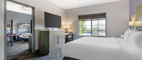Habitación de hotel con una cama grande, un escritorio con silla, un televisor montado en la pared y una ventana con vistas al exterior.