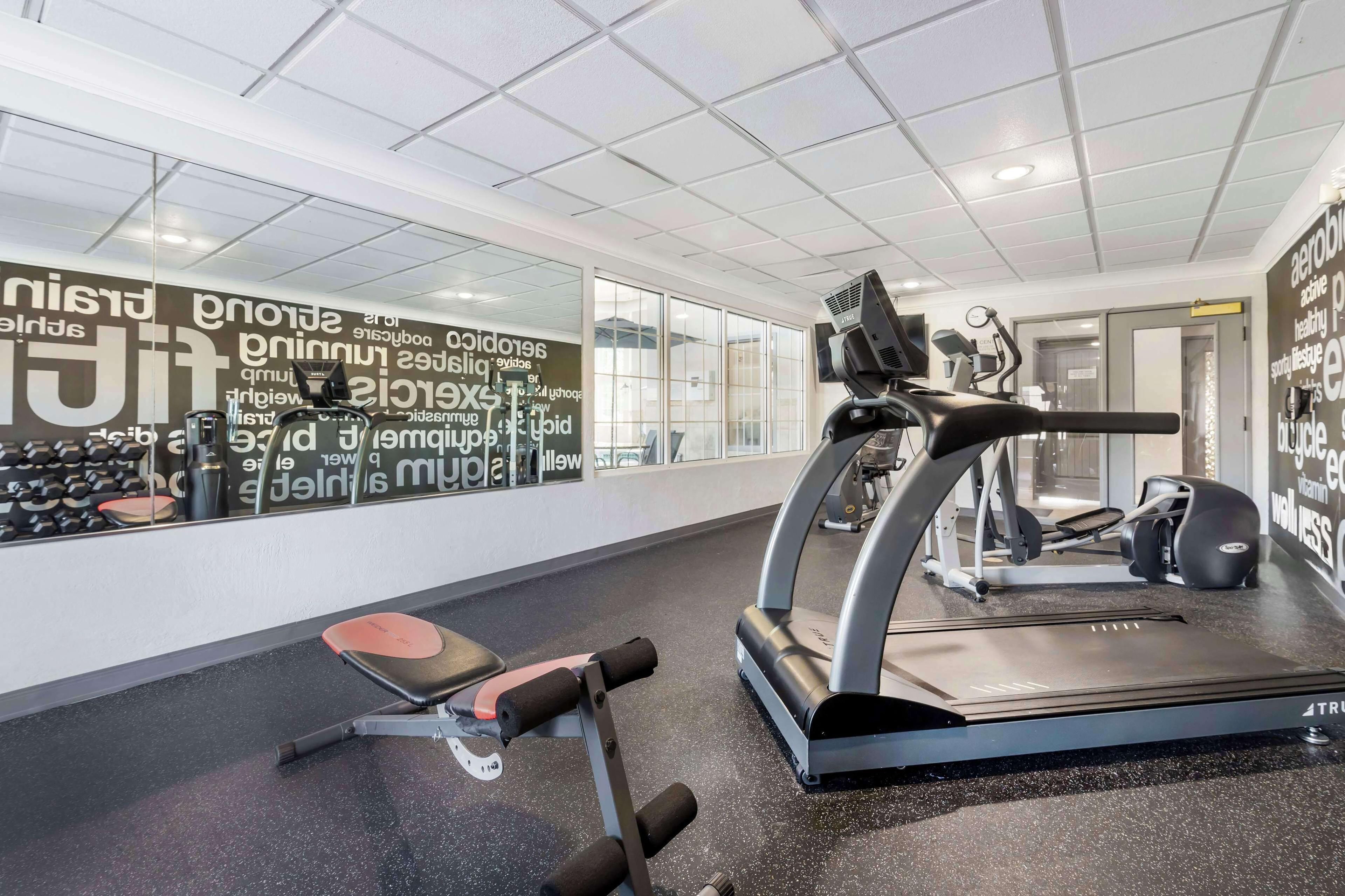 Ein Fitnessstudio mit Cardiogeräten, Gewichteinlagen und einer Wand mit motivierenden Sprüchen.