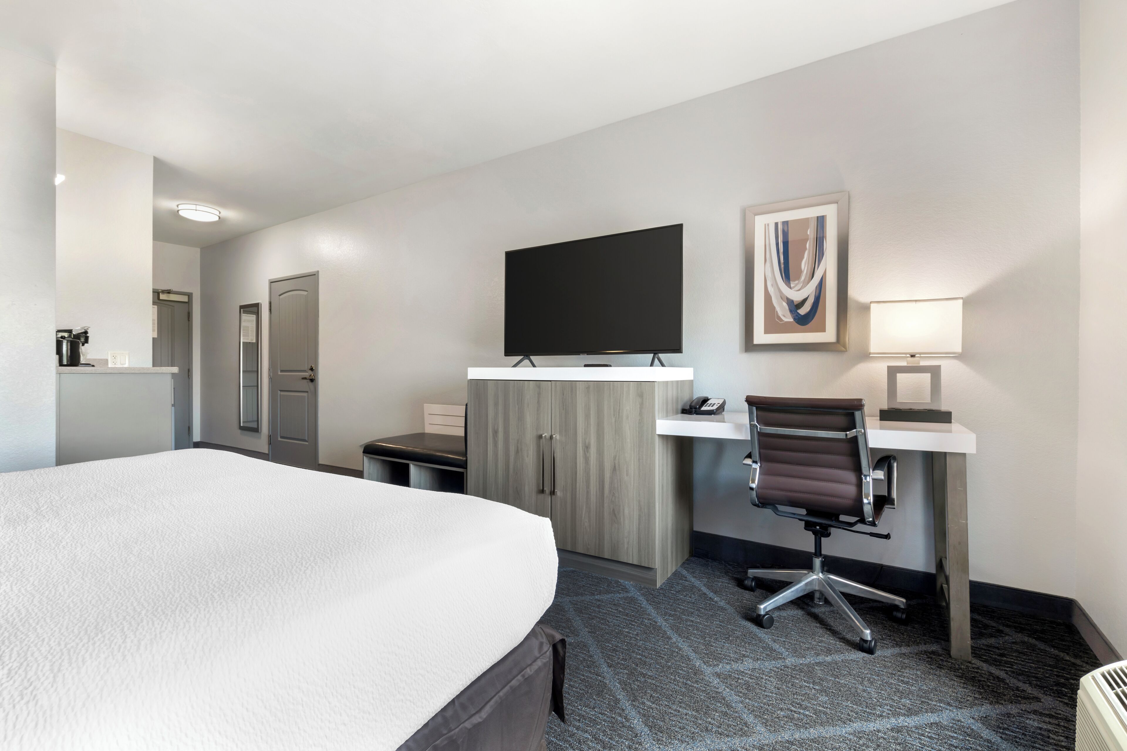 A hotel room with a large bed, a desk with a computer, a chair, a television, and a painting on the wall.