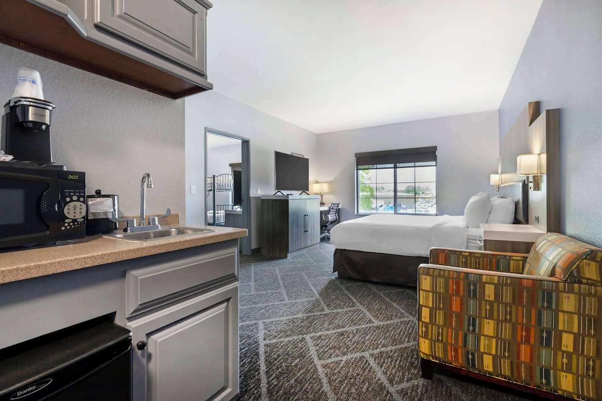 A hotel room with a kitchenette, a bed, a sofa, a desk, and a TV.