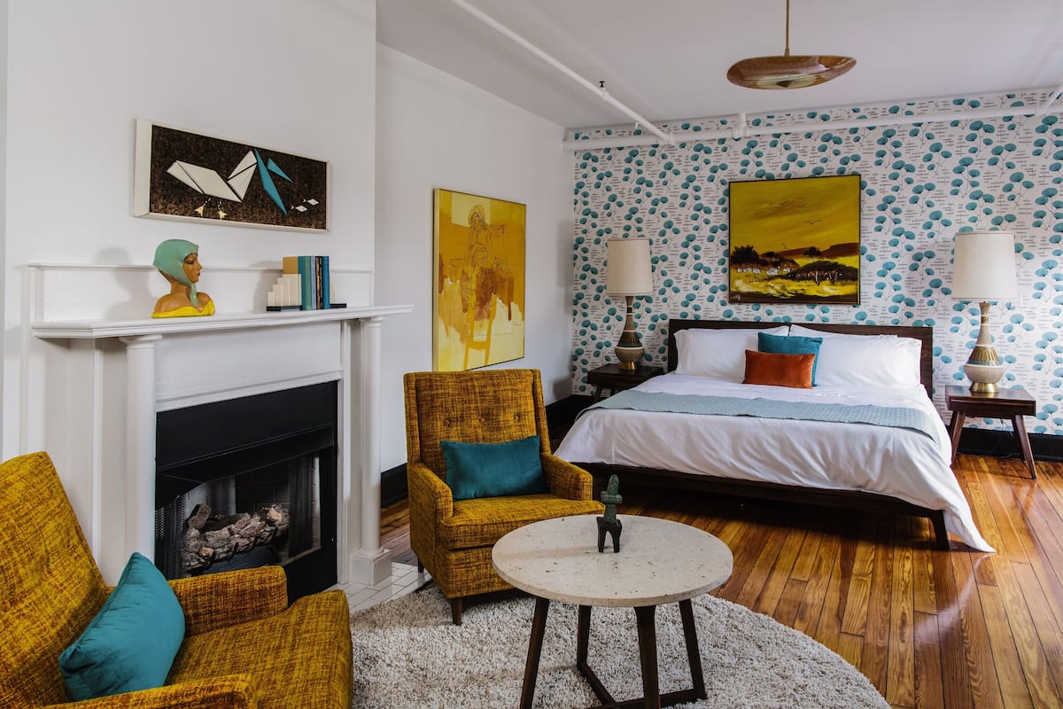 Ein Schlafzimmer mit einem Bett, zwei Sesseln, einem Kamin und Kunstwerken an den Wänden.
