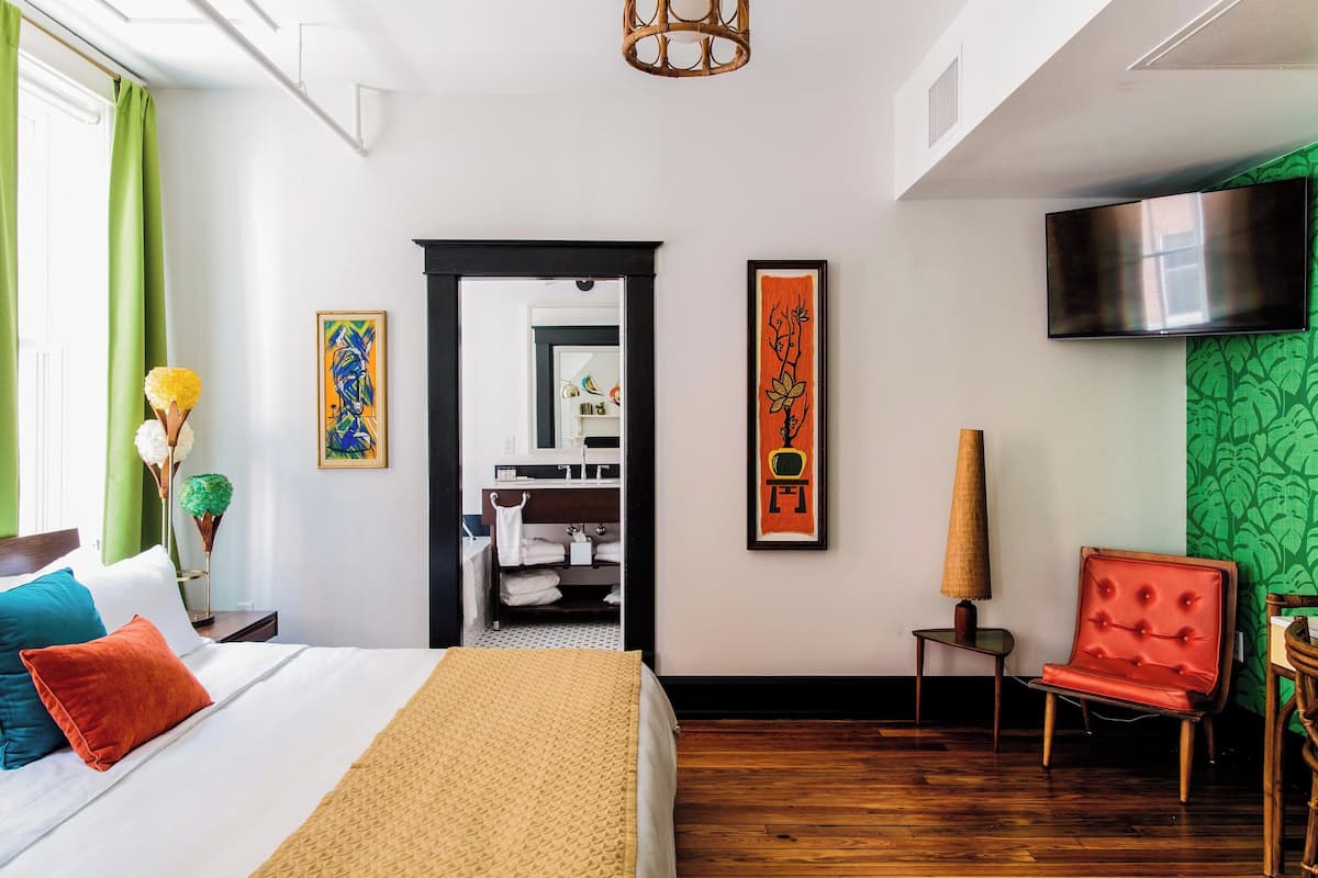 Ein Hotelzimmer mit Bett, Sessel, Fernseher und Bildern an der Wand.