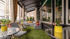 A modern outdoor seating area with a glass table, wicker chairs, a grey sofa, and yellow planters. - The Dwell Hotel, a Member of Design Hotels (Chattanooga)