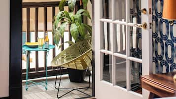 A room with a wooden floor, a green chair, a small table with a yellow tray, a potted plant, and a door with a patterned wallpaper.