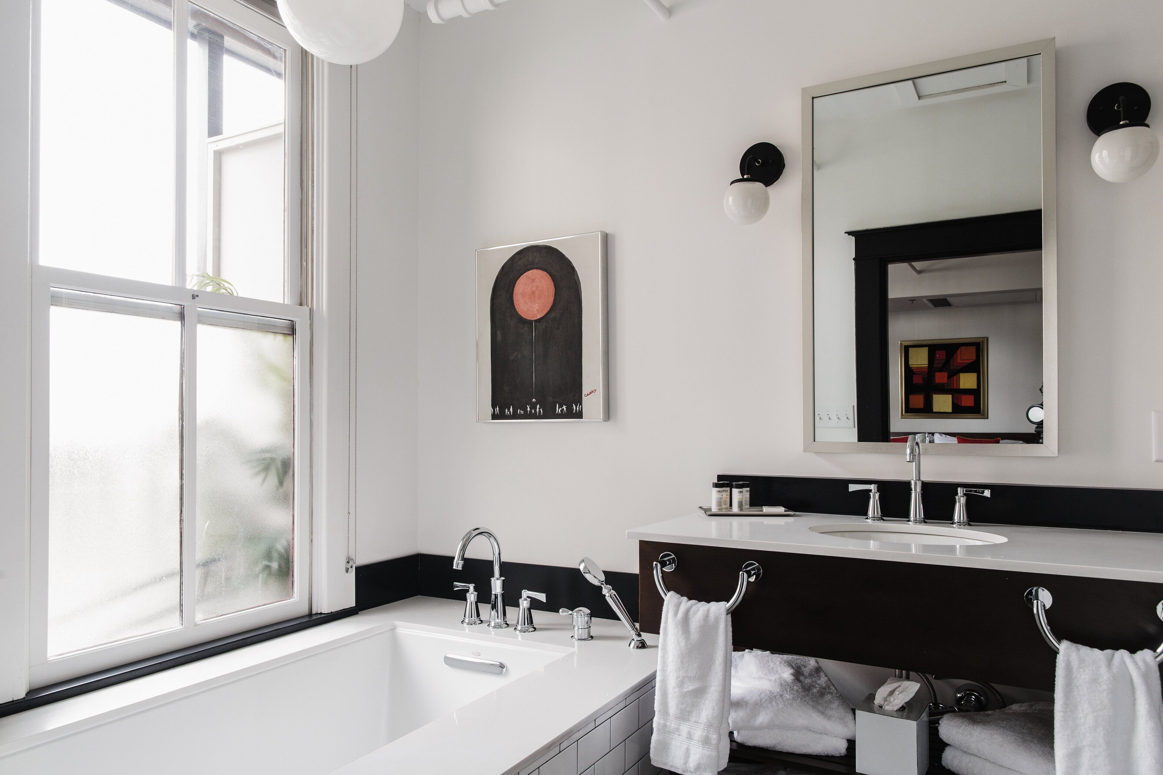 A modern bathroom with a large window, a bathtub, a double sink, and a mirror above the sink.