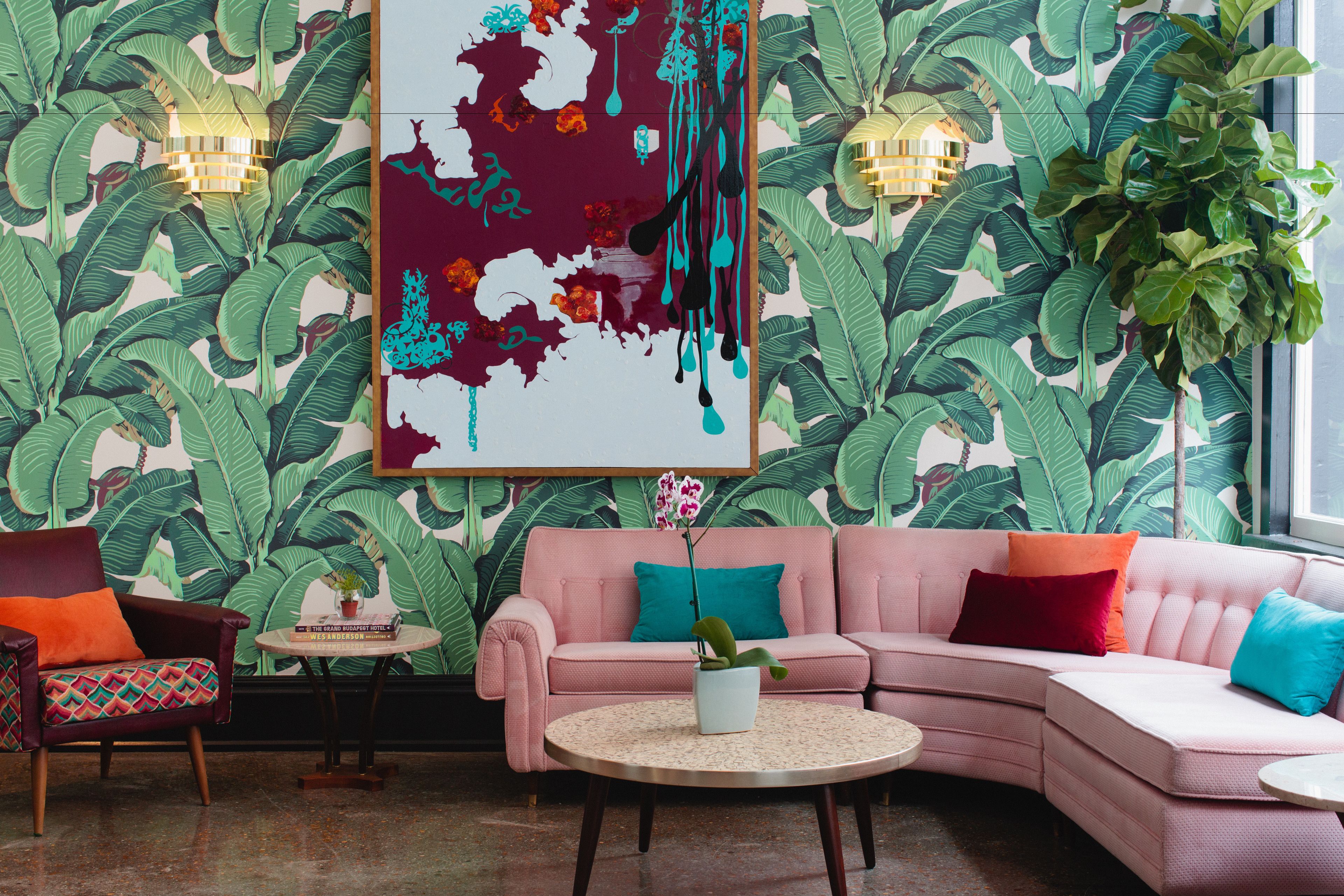 A room with a pink sofa, a small round table with a plant, and a large abstract painting on the wall.