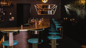 A bar area with a long counter, blue bar stools, and a variety of bottles on shelves. - The Dwell Hotel, a Member of Design Hotels (Chattanooga)