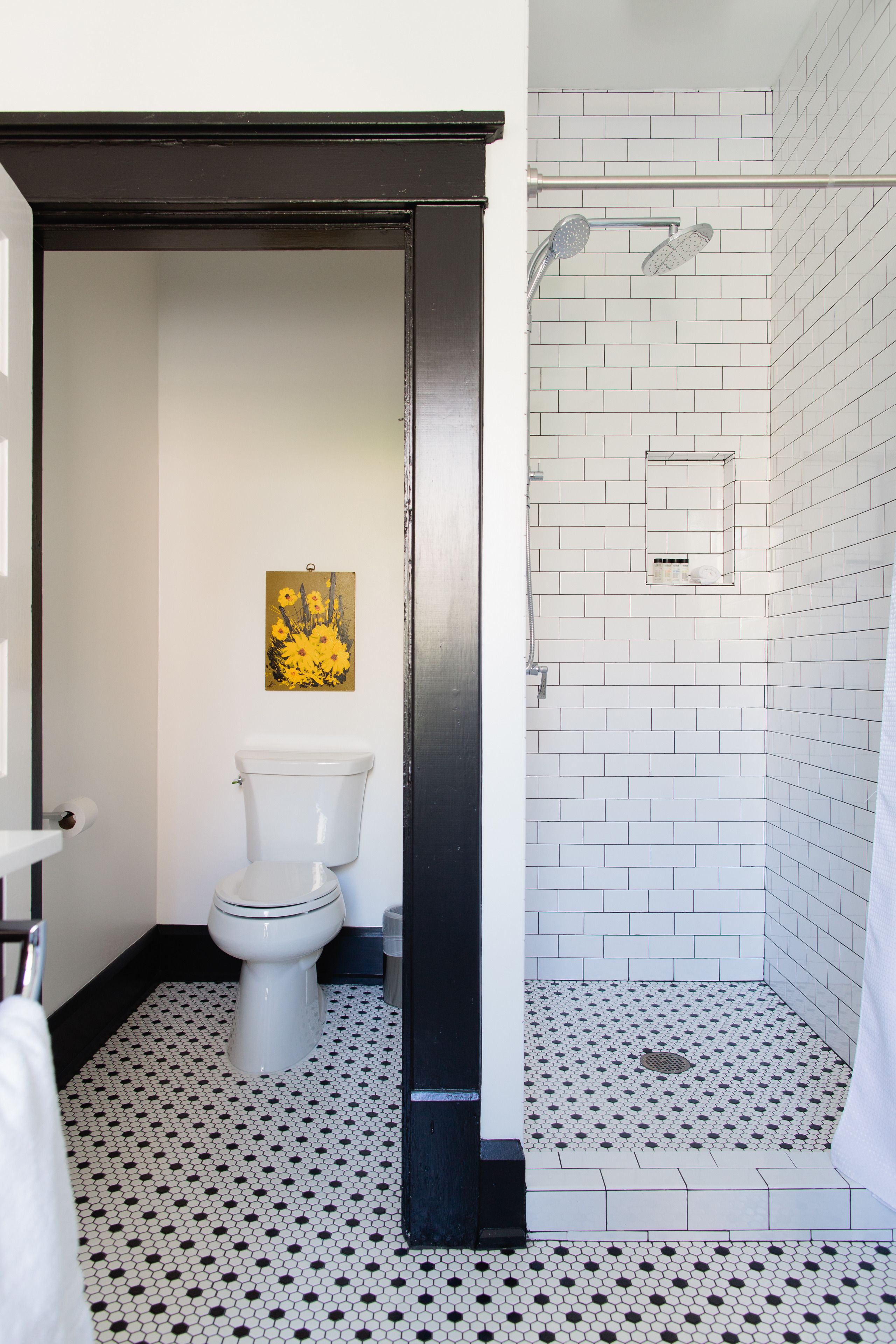 Une salle de bain avec des toilettes, une douche aux murs recouverts de carreaux blancs et un sol à motifs noir et blanc.
