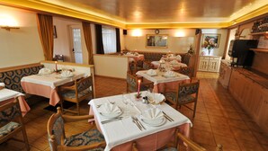 A restaurant with tables set for dining, wooden chairs, and a bar area. - Cristallo (San Giovanni di Fassa)
