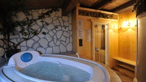 A hot tub in a wooden cabin with stone walls and a wooden door. - Cristallo (San Giovanni di Fassa)
