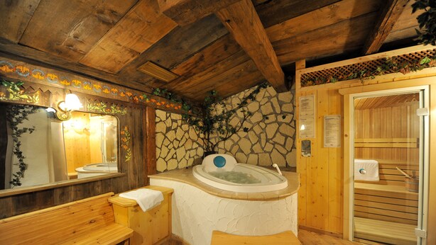A wooden sauna room with a stone wall, a bench, and a wooden bench. - Cristallo (San Giovanni di Fassa)