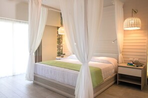 A bedroom with a bed, white curtains, a bedside table with books, and a wall-mounted lamp.