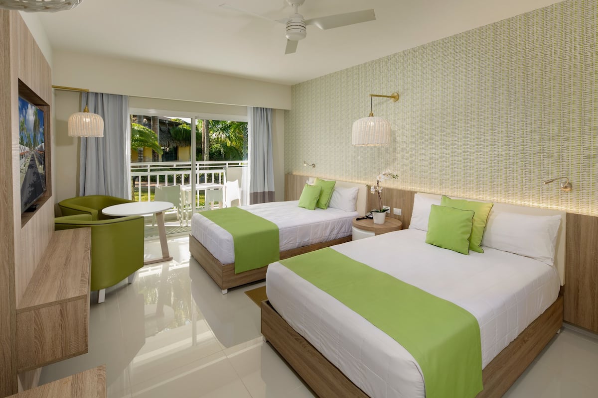 A hotel room with two beds, a balcony, a dining area, and a TV.