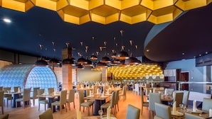 Un restaurante moderno con paneles hexagonales en el techo, varias mesas de comedor e iluminación colgante.