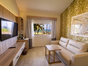 A modern living room with a TV, a sofa, a coffee table, and a view of the beach.