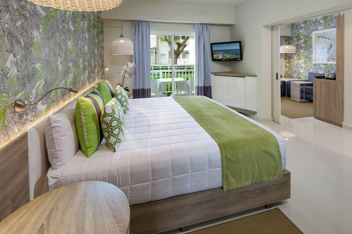A modern bedroom with a large bed, a TV, and a balcony with a view.