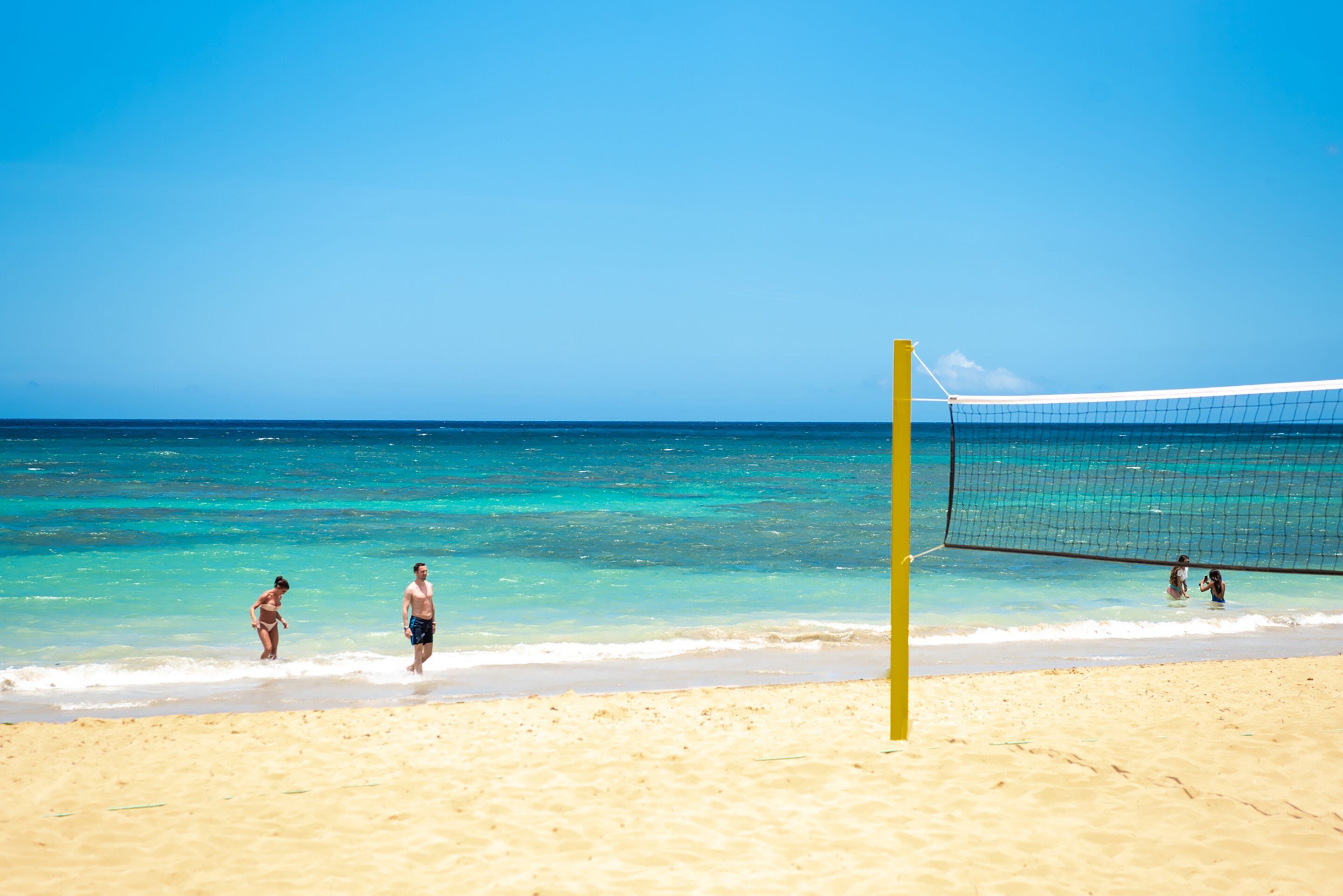 Ett nät för strandvolleyboll på en sandstrand med kristallklart blått vatten.
