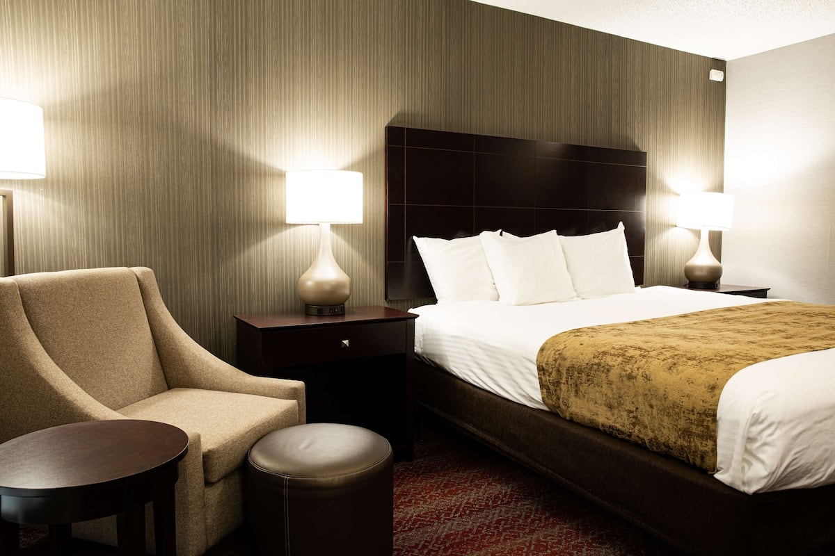 A hotel room with a bed, a chair, a small table, and two bedside lamps.