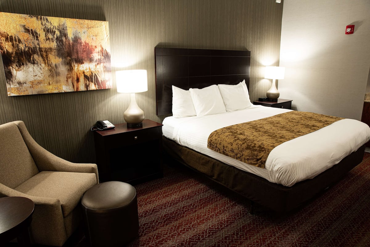 A hotel room with a large bed, two bedside tables with lamps, a chair, and a red patterned carpet.