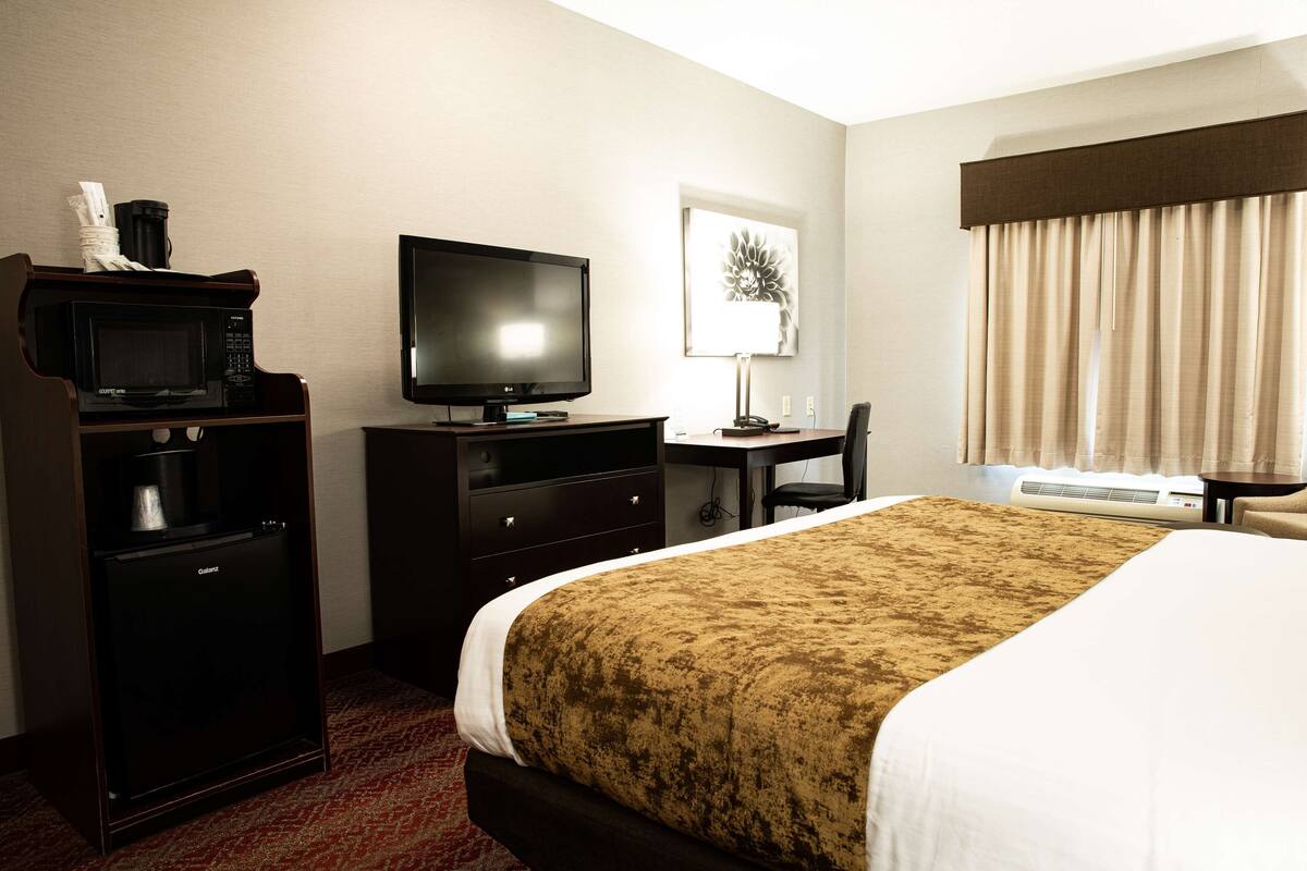 A hotel room with a bed, a desk with a computer, a television, a microwave, and a coffee maker.