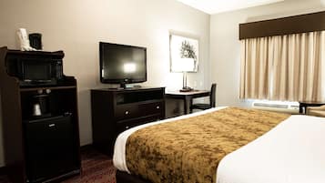 A hotel room with a bed, a desk with a computer, a television, a microwave, and a coffee maker.