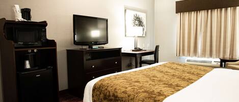A hotel room with a bed, a desk with a computer, a television, a microwave, and a coffee maker.
